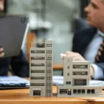 due persone parlano ad una scrivania con dei modellini di palazzi